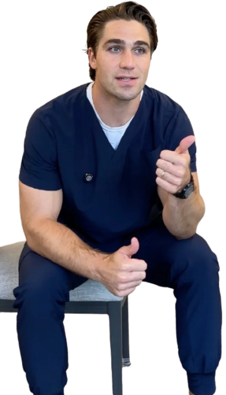 Robbie Peck, in navy scrubs, sitting on a stool and talking to the camera